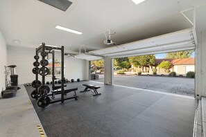 A spacious indoor gym with a squat rack, bench press, and free weights. - Pickleball Main House | Pool | Hot Tub | Arcade (Peoria)
