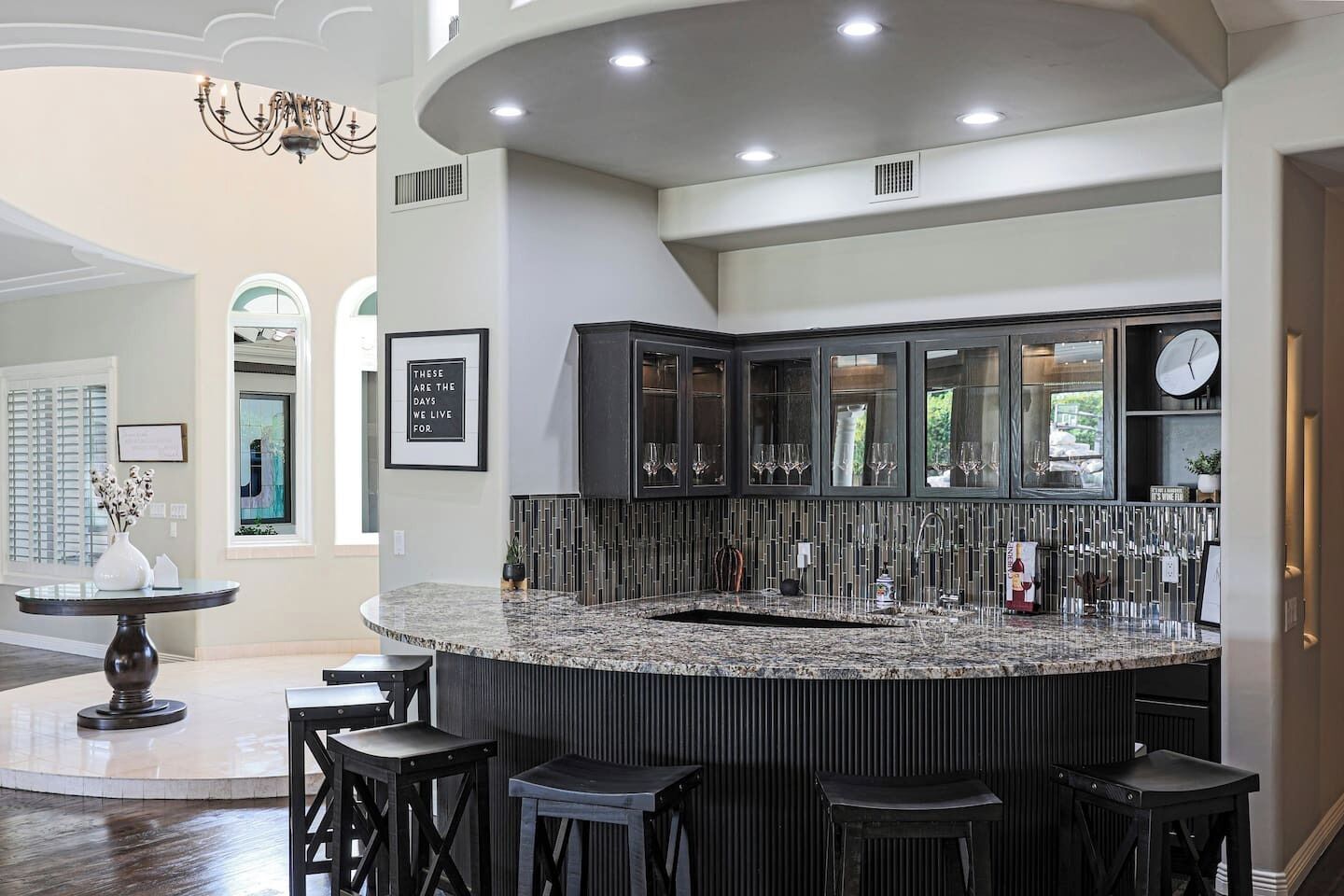 A modern kitchen with a curved granite countertop, dark cabinetry, and a built-in wine rack.