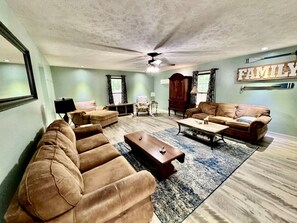 A spacious living room with a ceiling fan, a large wooden cabinet, and a 'FAMILY' sign on the wall.
