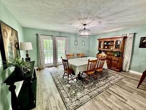 A dining room with a table and chairs, a chandelier, a wooden cabinet, and a large window with curtains.