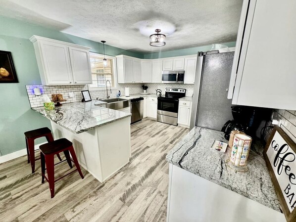 A kitchen with white cabinets, a granite countertop, a stainless steel refrigerator, and a coffee station.
