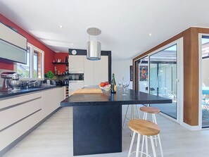 Een moderne keuken met een centraal eiland, barkrukken en een eethoek met een glazen deur naar buiten.