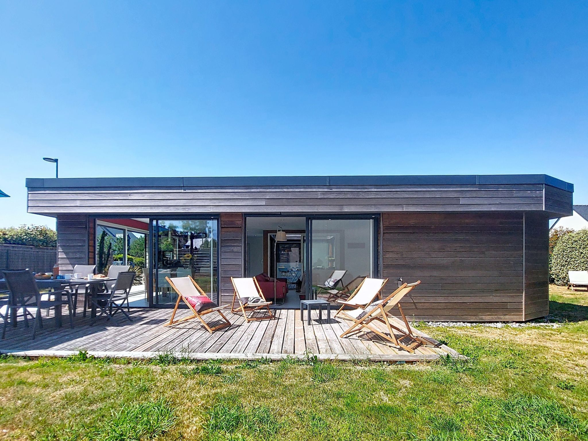 Ein modernes Haus mit einer Terrasse, Sitzgelegenheiten im Freien und einem Eingang mit Glastür.