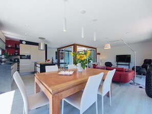 Eine moderne Küche mit Essbereich, ein Wohnzimmer mit rotem Sofa und einem Fernseher.
