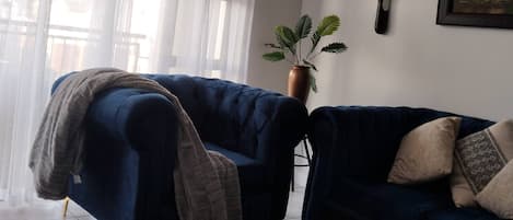 A living room with a blue sofa, a coffee table, a potted plant, and a framed picture on the wall.