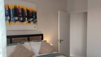 A bedroom with a bed, pillows, a headboard, a painting, a door, and a light fixture.