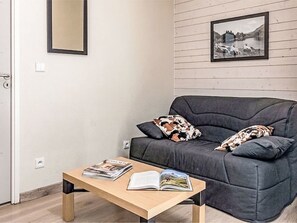 A modern living room with a dark grey sofa, two patterned cushions, a wooden coffee table with magazines, and a framed picture on the wall. - Les Chalets d'Ax by Interhome (Ax-Les-Thermes)
