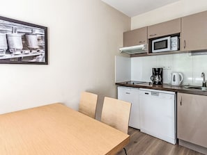 A compact kitchen with a microwave, coffee maker, and dishwasher. There is a wooden table with chairs and a framed picture on the wall. - Les Chalets d'Ax by Interhome (Ax-Les-Thermes)