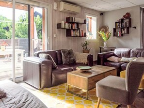 A living room with a sofa, armchair, and coffee table, a bookshelf, and a view through a sliding glass door. - Les Chalets d'Ax by Interhome (Ax-Les-Thermes)