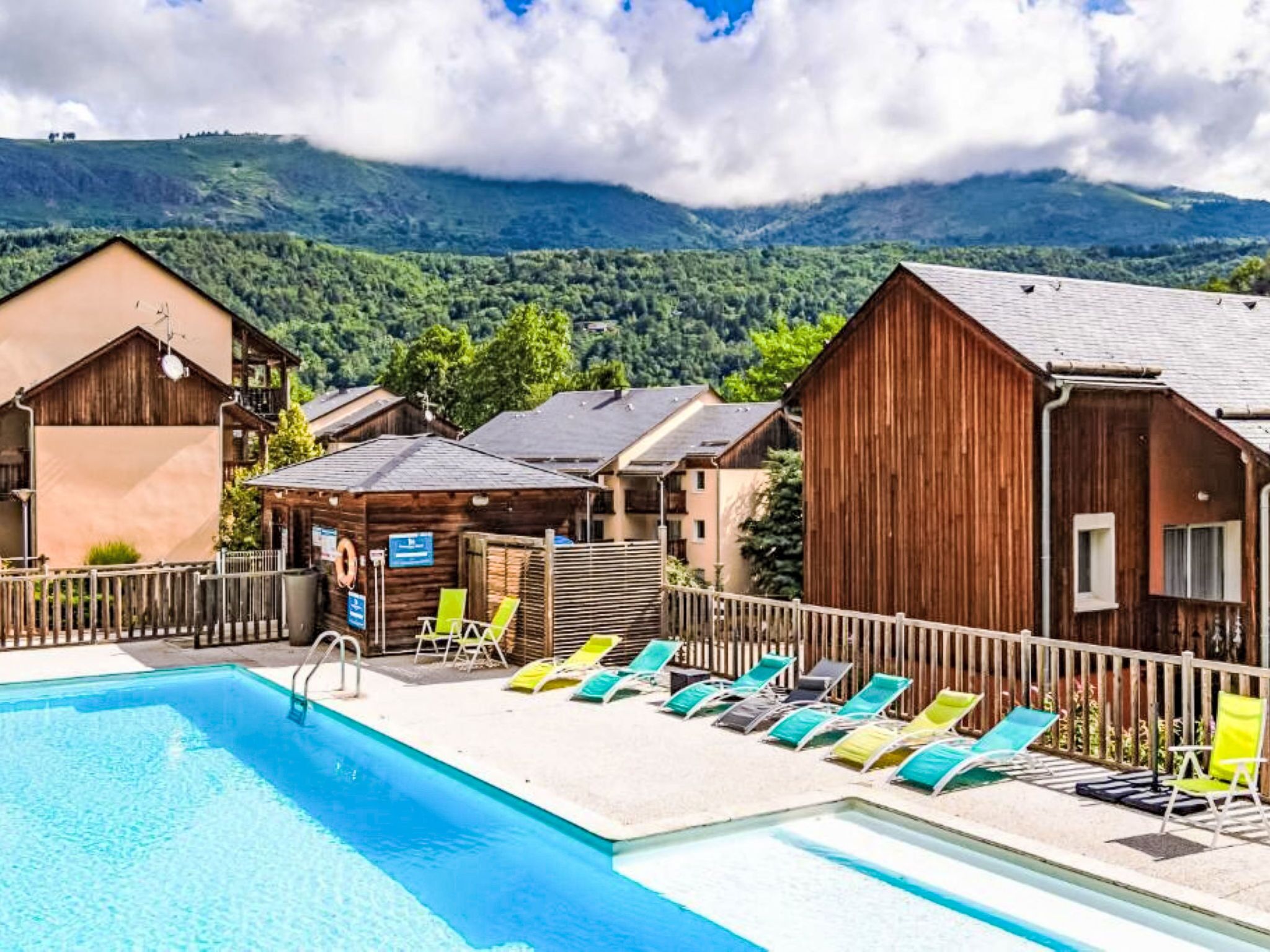 A swimming pool with lounge chairs and wooden cabins in a mountainous area.