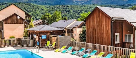 A swimming pool with lounge chairs and wooden cabins in a mountainous area.