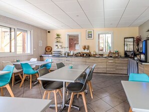 A modern dining area with tables and chairs, a kitchen area with appliances and a refrigerator, and a view through a doorway. - Les Chalets d'Ax by Interhome (Ax-Les-Thermes)