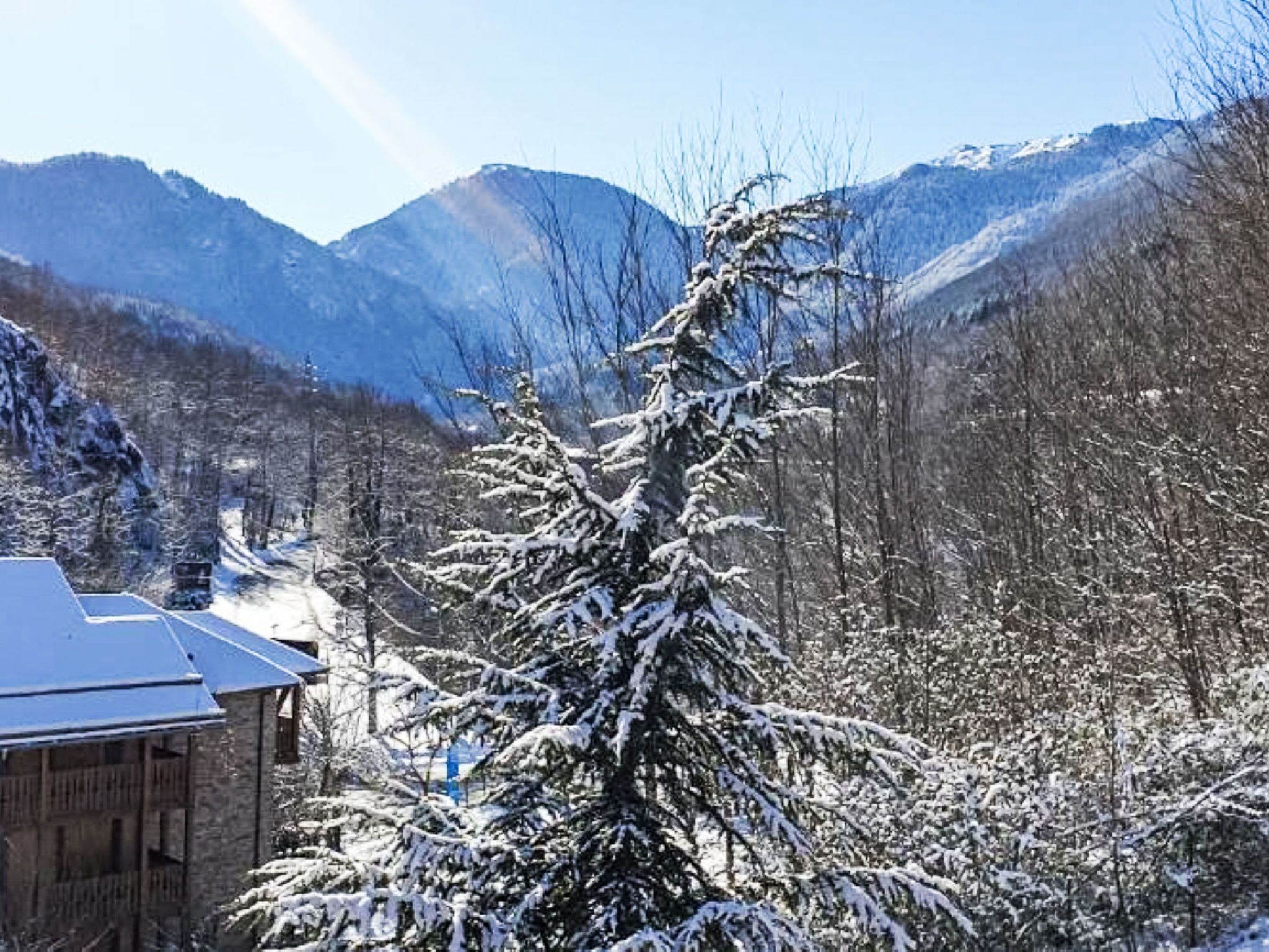 Paisagem coberta de neve com montanhas ao fundo e um edifício com telhado inclinado em primeiro plano.