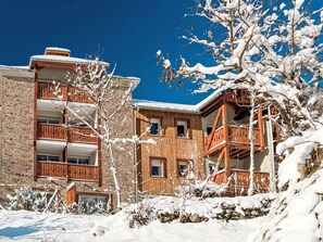 Un edificio a più piani con balconi, circondato da alberi innevati e un cielo azzurro limpido.