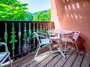 Un balcone con tavolo e sedie, un pavimento in legno e un recinto nero decorato con elementi vegetali.