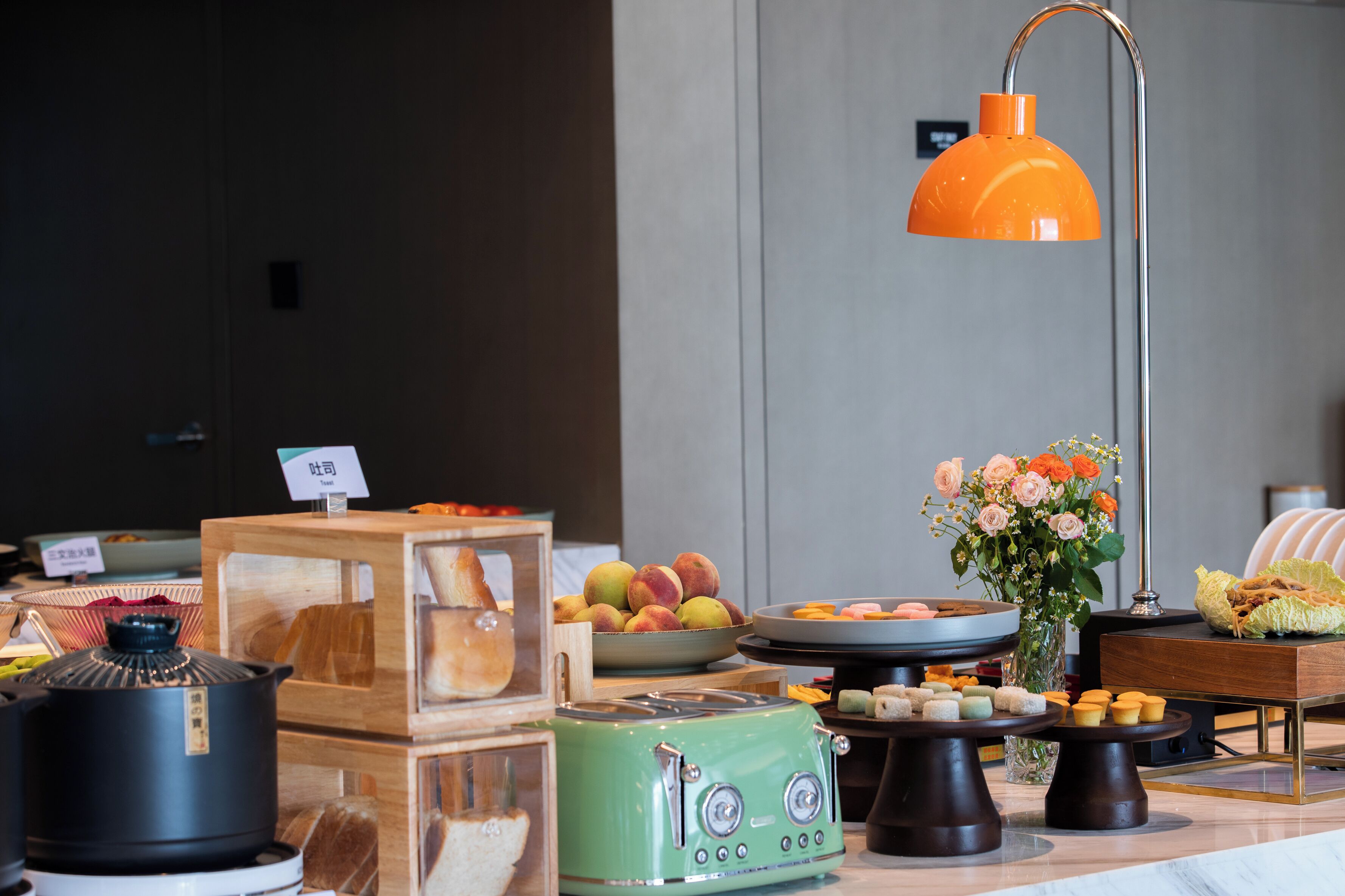 A buffet setup with various food items, a green toaster, and a vase with flowers.