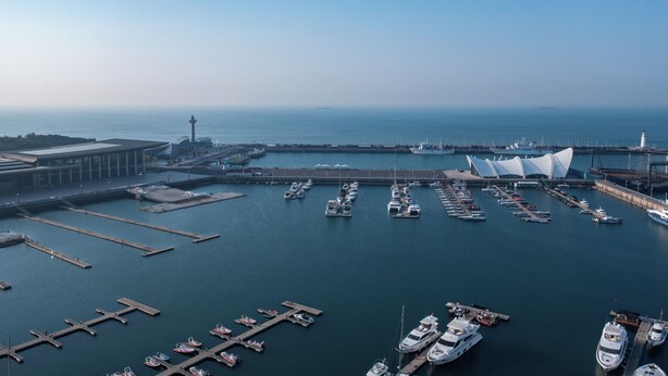 A marina with multiple docks and boats, a bridge, and a distinctive modern building with a curved roof. - Atour Hotel, Hisense Plaza, May Fourth Square, Qingdao (Qingdao)