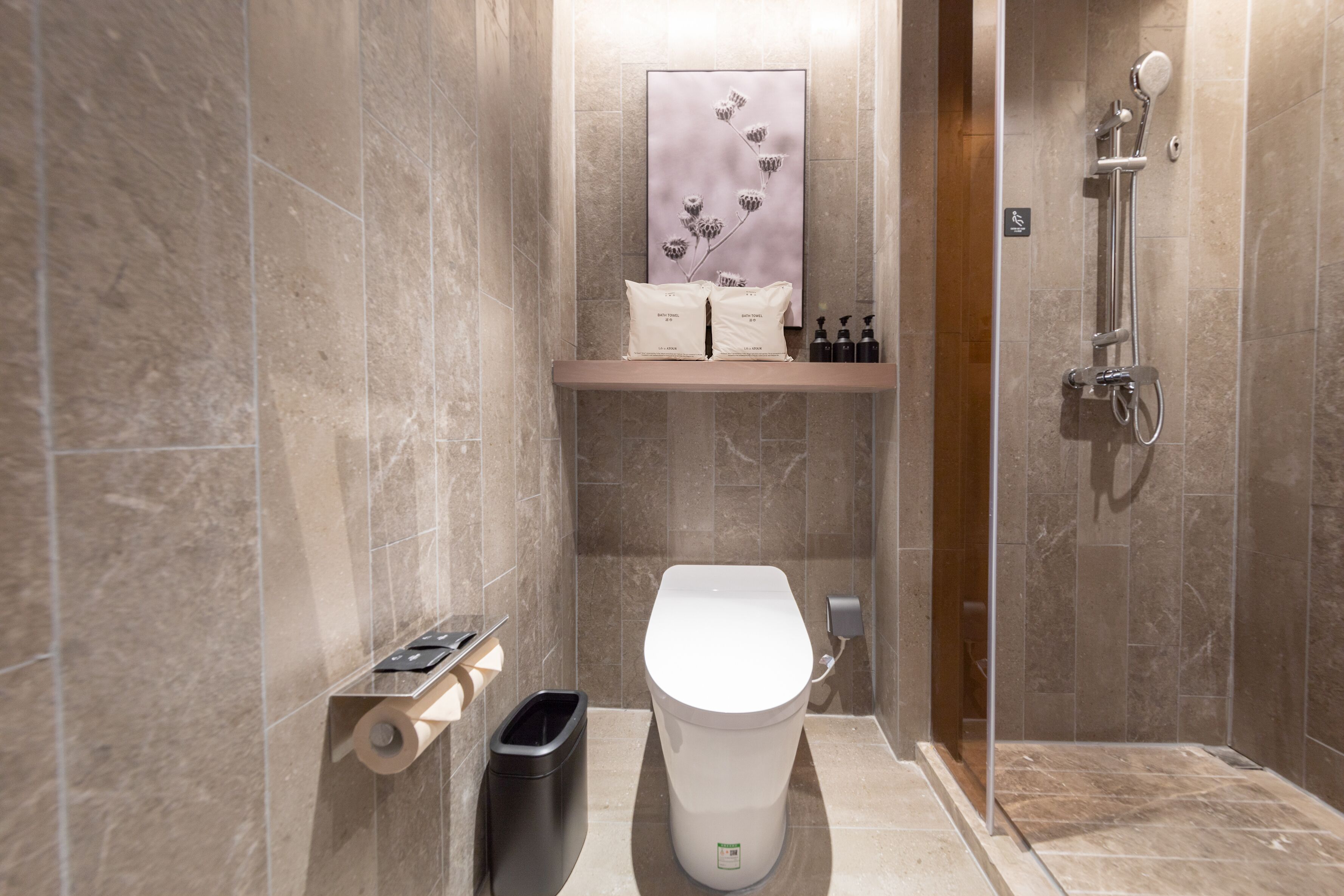 Een moderne badkamer met een toilet, een prullenbak, een douche en een plank met toiletartikelen.