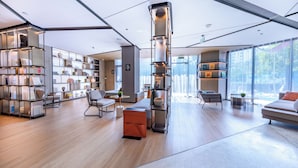 A modern interior with a central cylindrical light fixture, open shelving with books, and a seating area with a sofa and chairs. - Atour Hotel, Hisense Plaza, May Fourth Square, Qingdao (Qingdao)