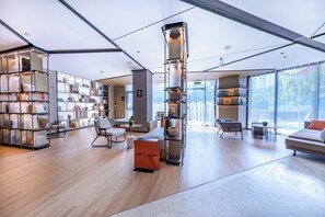 A modern interior with a central cylindrical light fixture, open shelving with books, and a seating area with a sofa and chairs. - Atour Hotel, Hisense Plaza, May Fourth Square, Qingdao (Qingdao)