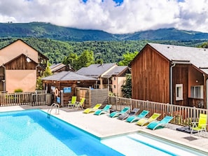 Ein Schwimmbecken mit Liegestühlen und Holzhütten in einer gebirgigen Landschaft.