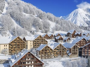 A snow-covered lodge with multiple wooden buildings, a mountain backdrop, and a clear sky. - Les Hauts de Vaujany by Interhome (Vaujany)