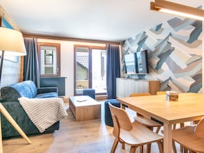 A modern living room with a sofa, a coffee table, a dining table with chairs, a TV, and a patterned wall. - Les Hauts de Vaujany by Interhome (Vaujany)