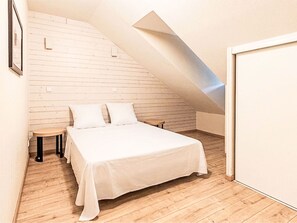 A bedroom with a sloped ceiling, a bed with white bedding, a small stool, and wooden flooring. - Les Chalets d'Ax by Interhome (Ax-Les-Thermes)