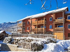 A multi-story building with balconies, a stone wall, and snow-covered ground. - Les Chalets d'Ax by Interhome (Ax-Les-Thermes)