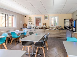 A modern dining area with tables and chairs, a kitchen area with appliances and a refrigerator, and a view through a doorway. - Les Chalets d'Ax by Interhome (Ax-Les-Thermes)