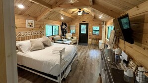 L’intérieur d’un chalet en bois comprend un lit, un coin salon, un téléviseur et une cheminée.