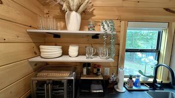 A compact kitchen with wooden walls, a built-in oven, and a window with a view of greenery.