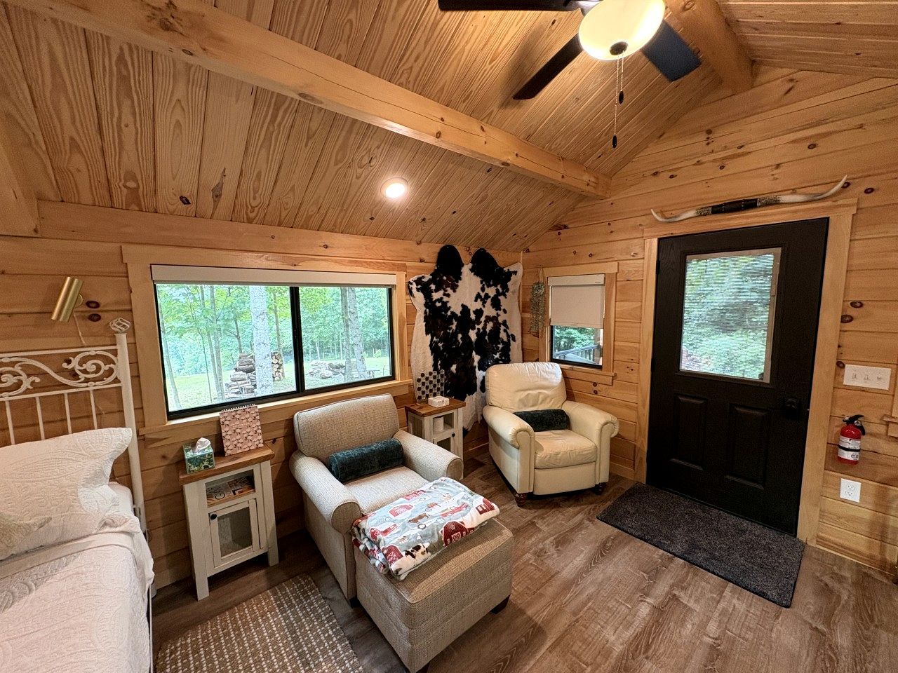 Interior acogedor de una cabaña con una cama, dos sillones, una mesita y un televisor.