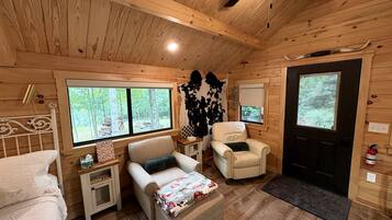 Interior acogedor de una cabaña con una cama, dos sillones, una mesita y un televisor.