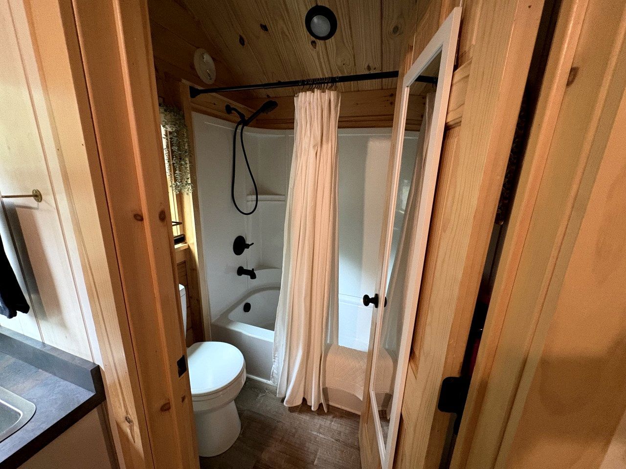 A wooden interior with a white toilet, a bathtub, and a shower curtain.