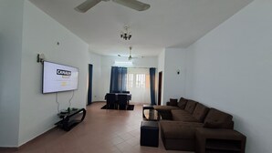 Una sala de estar con ventilador de techo, un televisor montado en la pared, un sofá marrón y una zona de comedor con mesa y sillas.