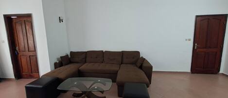 A living room with a brown sectional sofa, a glass-top coffee table, and two black ottomans.