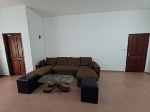 Ein Wohnzimmer mit einem braunen Ecksofa, einem Couchtisch mit Glasplatte und zwei schwarzen Hocker.