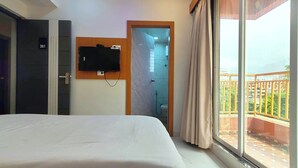 Ein Hotelzimmer mit Bett, einem an der Wand montierten Fernseher, einem Badezimmer mit Dusche und einem Balkon mit Geländer.
