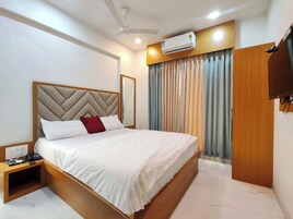 A hotel room with a bed, a ceiling fan, an air conditioning unit, a bedside telephone, and a wardrobe.