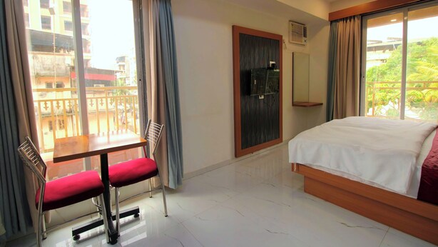 Habitación de hotel con cama, una mesa y una silla, ventana con cortinas y vista a edificios.