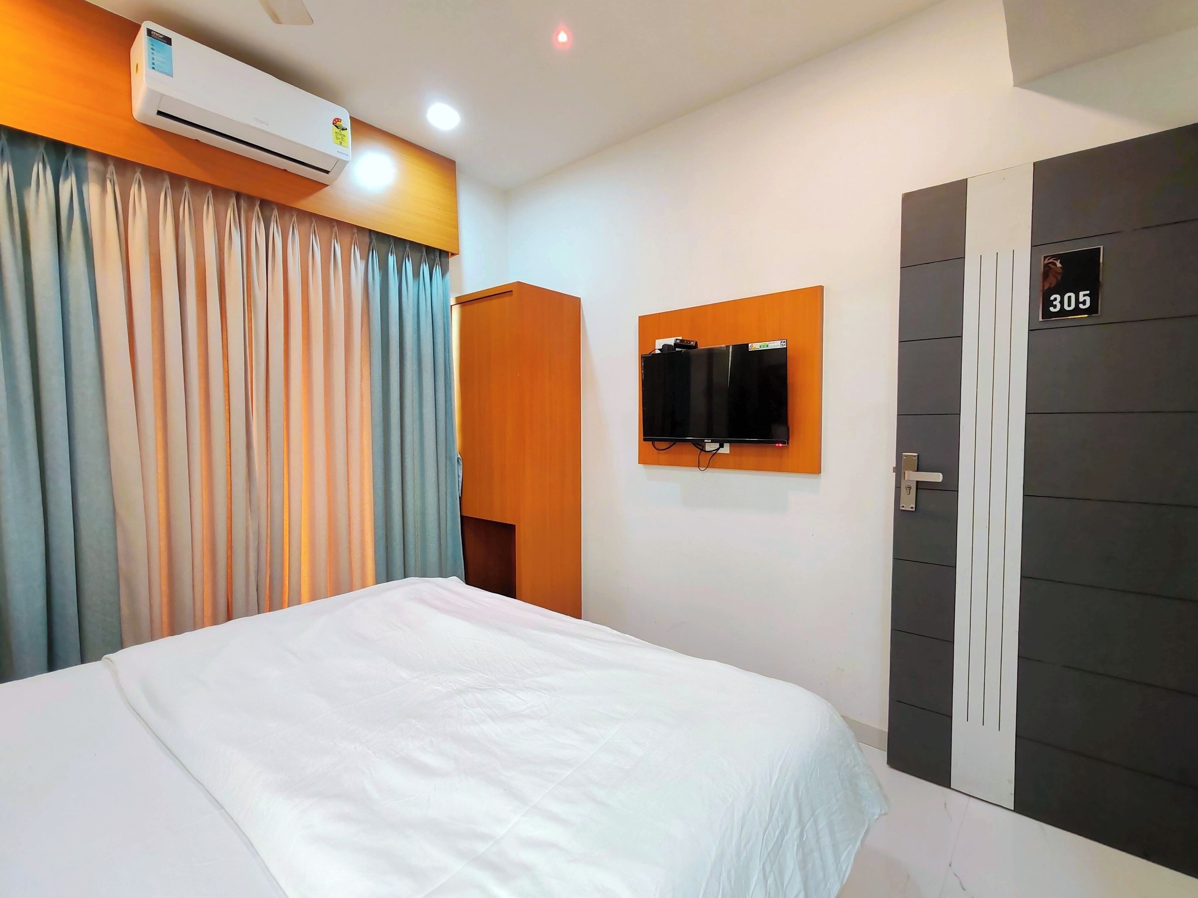 Een hotelkamer met een bed, een airconditioning, een televisie en een deur met een nummer.