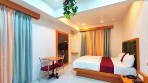 A hotel room with a bed, a desk with a chair, a TV, and a ceiling fan.