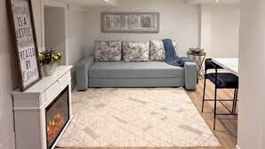 A modern living room with a sofa, a fireplace, a dining area, and a ceiling with recessed lighting. - Executive 1BR Suite | Express Transit to Downtown & Airport | Fast Wi-Fi (Toronto)