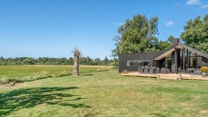 Ein modernes Haus mit Terrasse, umgeben von einer grünen Wiese und Bäumen.