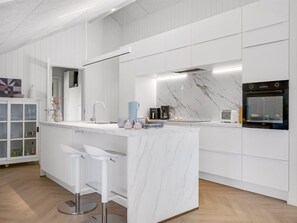 A modern kitchen with white cabinetry, a marble countertop, and stainless steel appliances. - "Tameran" -  from the sea by Interhome (Hals)