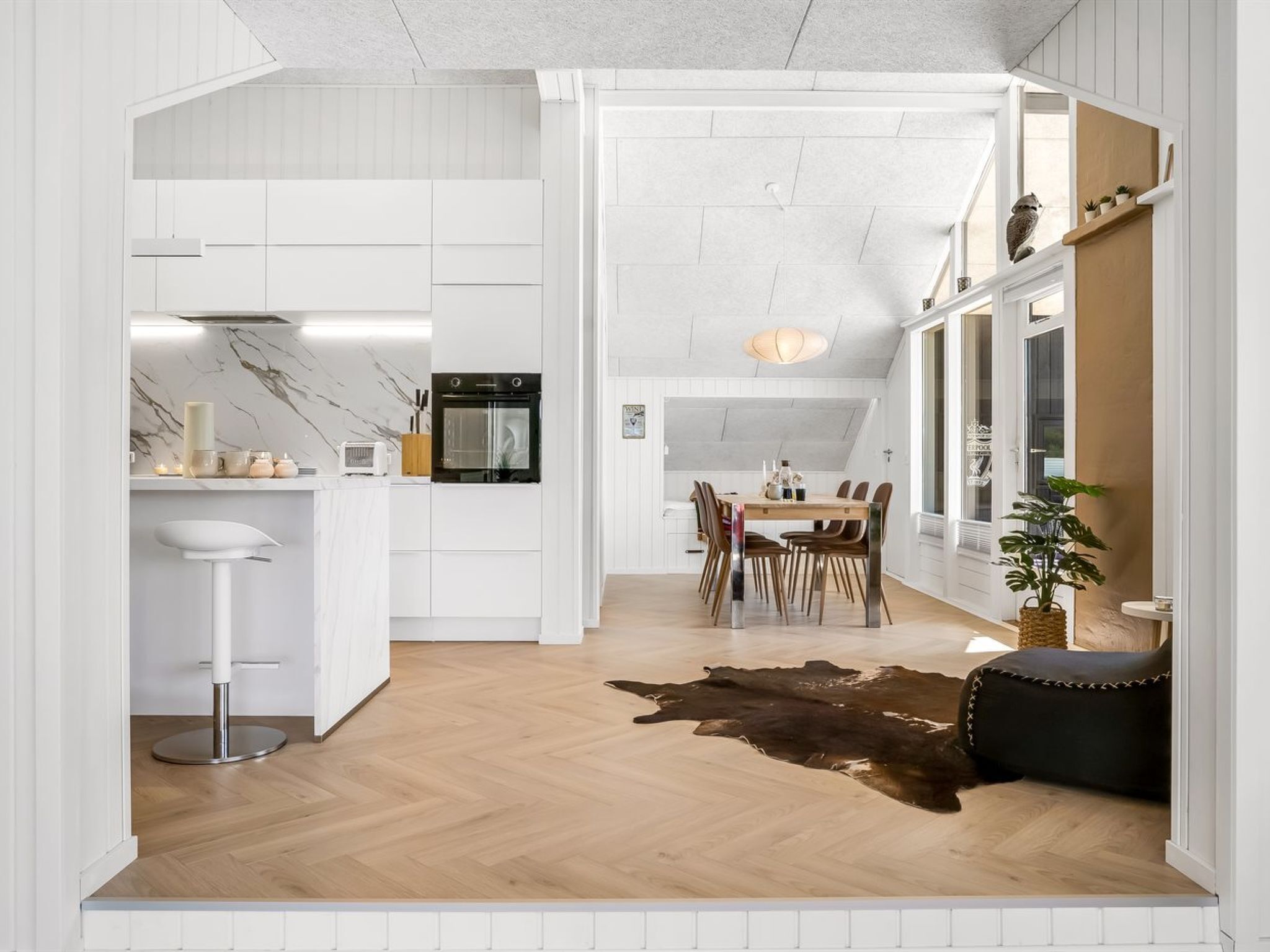 Una cocina moderna con armarios blancos, una isla central y un comedor con mesa y sillas de madera.