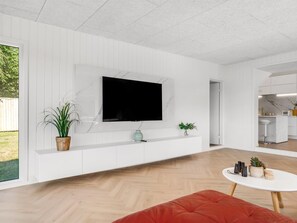 Una sala de estar moderna con un televisor de pantalla plana montado en una pared blanca, piso de madera y un sofá rojo.