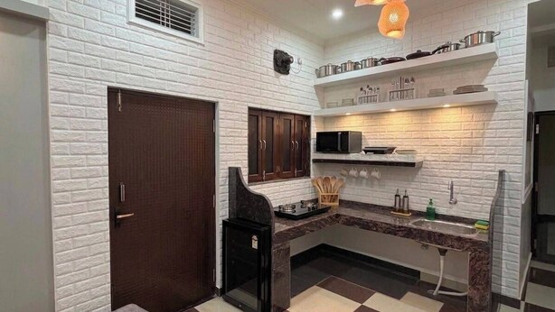 Una cocina con paredes de ladrillo blanco, una puerta oscura, un microondas y un lavabo.