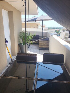 A balcony with a glass table, two cushioned chairs, a potted plant, and a mop leaning against the wall. - Luminous Cocoon - All-Around Comfort - Sleeps 4 to 6 (Montpellier)